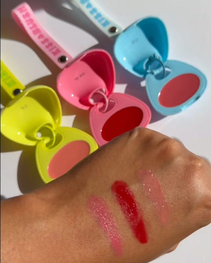Glossy pink and red swatches beside open Kiss & Blush compacts